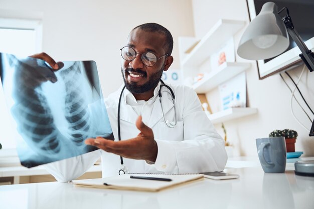 Médico de contenido señalando con la palma de la mano una película de tórax