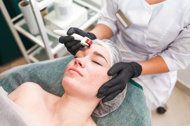 Médico cosmetologista faz o procedimento de massagem facial usando um rolo dermo. mulher no salão de beleza durante o procedimento de mesoterapia com mesoscooter