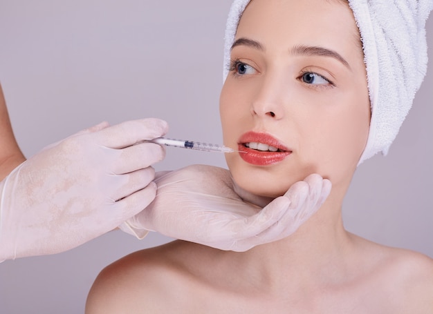 Un médico cosmetólogo hace una inyección en los labios de una mujer joven.