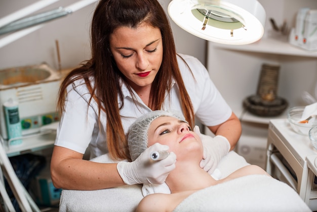 Foto el médico-cosmetólogo realiza un procedimiento de limpieza por ultrasonido de la piel facial.