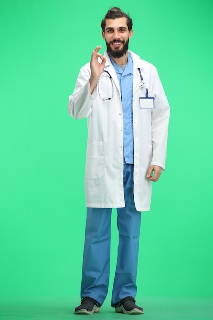 Un médico de cuerpo entero en un fondo verde muestra una señal de OK