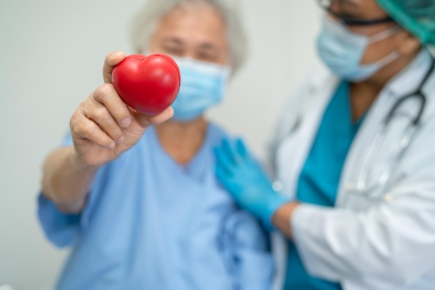 El médico le da un corazón rojo a una anciana asiática o a una anciana, una paciente, un concepto médico fuerte y saludable