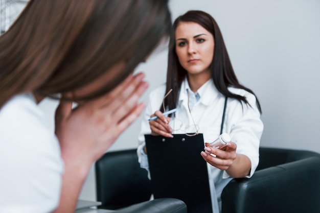 El médico le da medicamentos al paciente que llora Una mujer joven tiene una visita con una doctora en una clínica moderna