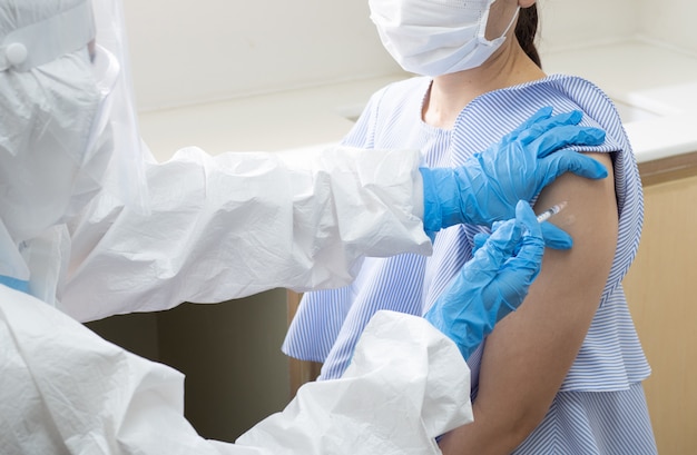 Foto médico da mulher asiática em traje de proteção individual injetar tiro vacina para estimular a imunidade do paciente mulher de beleza em risco de infecção por coronavírus.