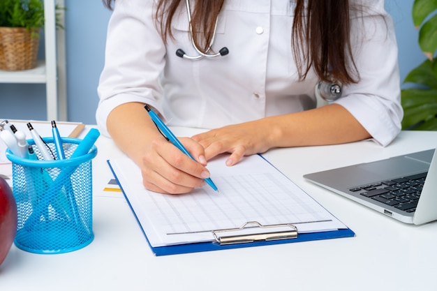 Médico da mulher tomando notas na área de transferência enquanto está sentado em sua mesa no escritório