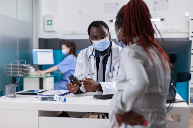 Médico dando botella de píldoras a la mujer embarazada con enfermedad en el consultorio médico. Paciente que espera al niño que recibe el matraz con medicamentos recetados del médico para tratar la enfermedad