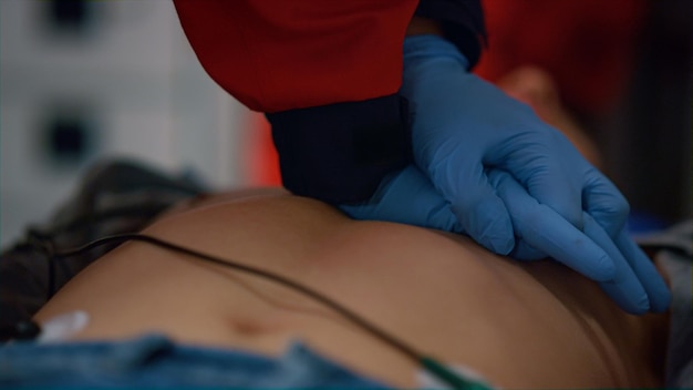 Médico de ambulância em close-up dando massagem cardíaca ao paciente em camisetas Paramedico profissional reanimando homem ferido Médico masculino irreconhecível dando primeiros socorros à vítima no carro de emergência