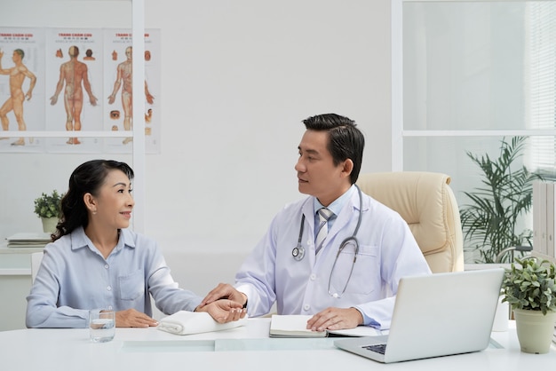 Médico de clínica geral conversando com um paciente sênior e medindo seu pulso antes do exame