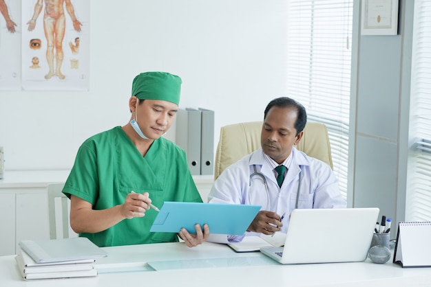 Médico de clínica geral sério e seu colega discutindo os exames médicos do paciente sentado à mesa do escritório