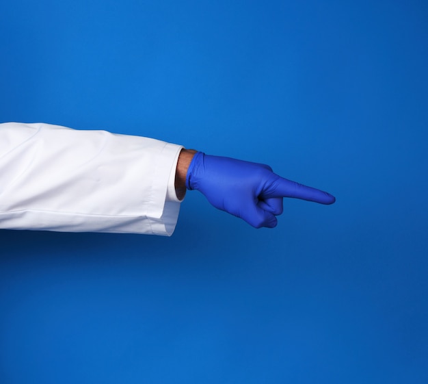 Médico de jaleco branco, usando luvas estéreis azuis, mostrando o gesto com a mão indicando o assunto, fundo azul