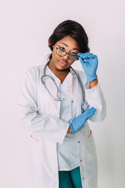 Médico de mulher afro-americana sorridente jovem em luvas médicas e roupas, isoladas no branco