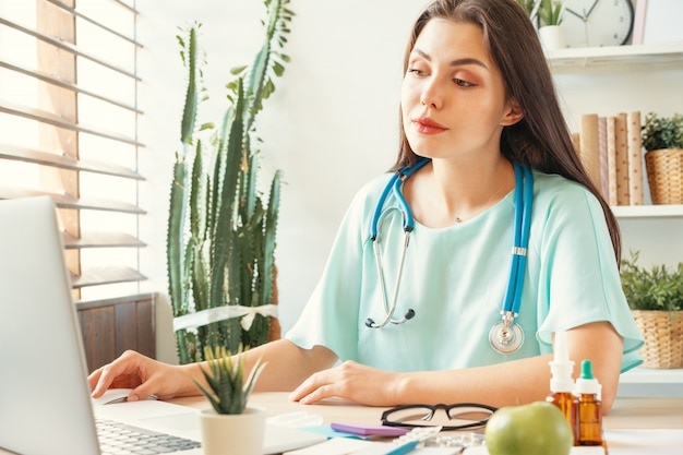 Médico de mulher bonita sentada à mesa no consultório médico