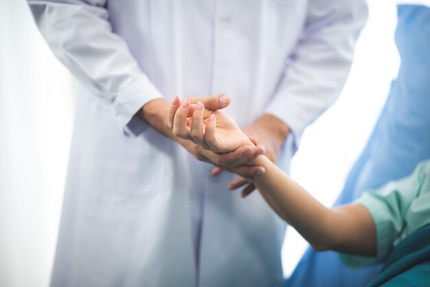 Médico de perto segurando a mão de um paciente representando conforto, esperança, calor e fechamento em uma sala de consultório médico