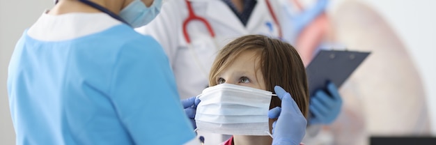 Médico de terno azul e máscara protetora colocou máscara protetora no rosto da menina.