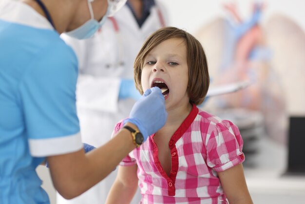 Médico de terno azul olhando para a garganta da criança com uma vara de madeira