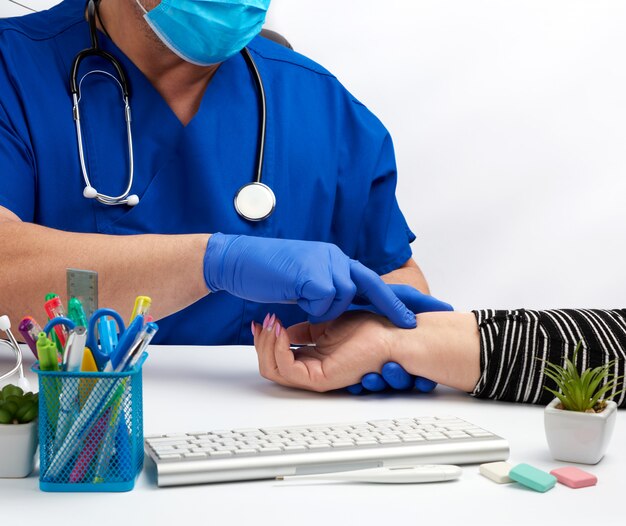 Médico de uniforme azul e máscara descartável mede o pulso da mulher na mão direita, o conceito de receber e consultar pacientes