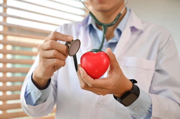 Foto médico de uniforme branco segurando estetoscópio e forma de coração vermelho doação de órgãos de saúde e conceito de cardiologia