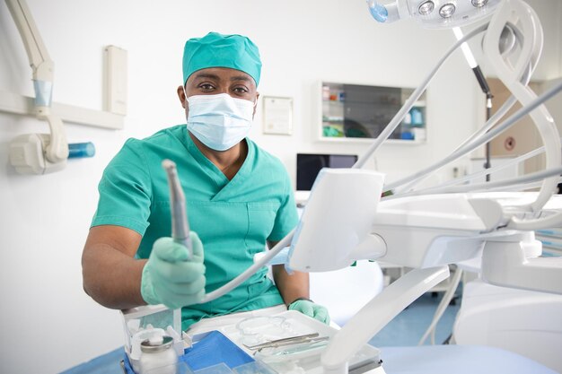 Médico dental en la clínica con un taladro dental en la mano y con una mascarilla quirúrgica