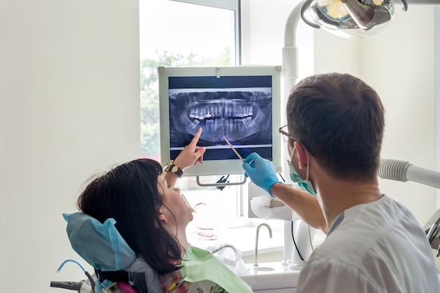 Médico dentista apontando no raio-x do paciente no monitor