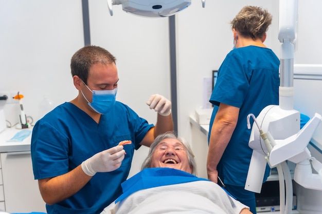 Médico dentista de la clínica dental pasando un buen rato con una anciana acostada en la mesa