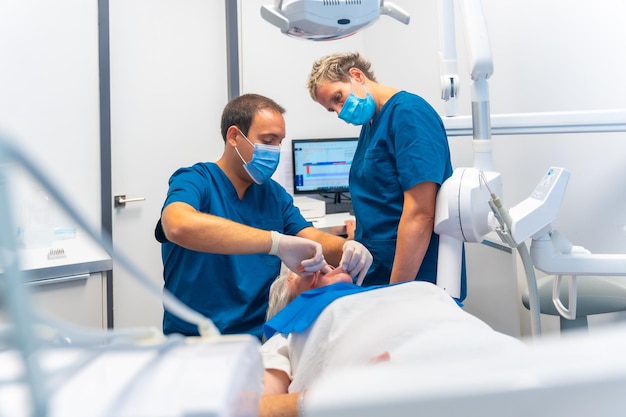 Médico dentista da clínica odontológica e assistente examinando os dentes de uma mulher idosa deitada na mesa