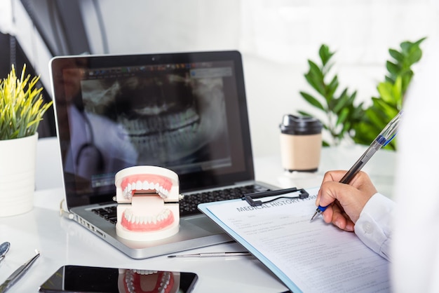 Médico dentista em uniforme escrevendo informações do paciente na lista de verificação de papelada na área de transferência