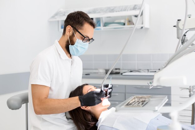 Médico dentista con gafas llenando los dientes de una paciente