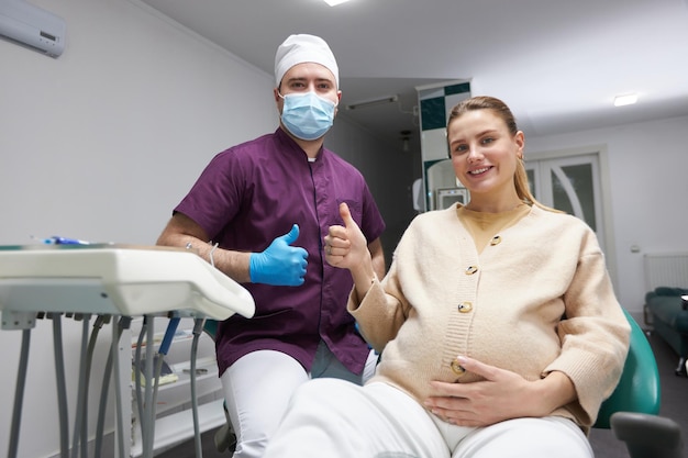 Foto médico dentista y mujer embarazada sonriendo mirando a la cámara después del chequeo dental