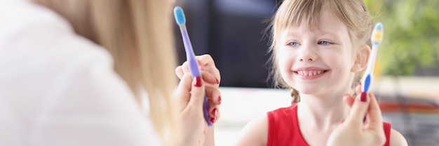 Foto médico dentista que ofrece a la niña dos cepillos de dientes para elegir en la clínica