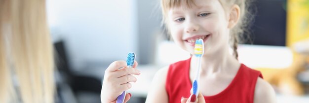 Médico dentista sosteniendo dos cepillos de dientes frente a una niña pequeña