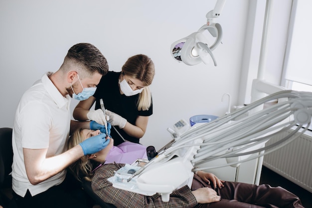 Médico dentista trata os dentes de uma linda jovem paciente A garota na recepção no dentista Médico dentista trata o dente