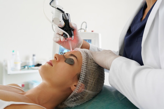 Médico dermatologista e cliente mulher durante o tratamento de recapeamento da pele a laser em uma clínica de estética médica