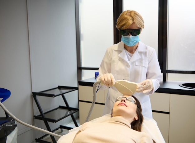 Médico dermatólogo cosmetólogo que brinda terapia láser facial para eliminar el vello, alisar la piel y tratar las manchas de la edad en la cara del paciente