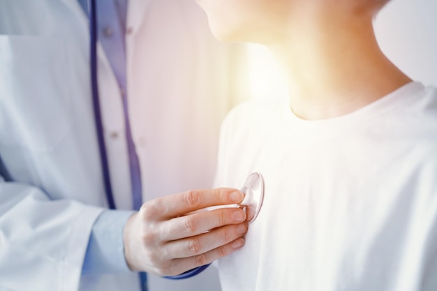 Médico desconhecido e paciente menino garoto na inspeção médica habitual. Médico trabalha usando estetoscópio, close-up. Medicina, conceitos de saúde