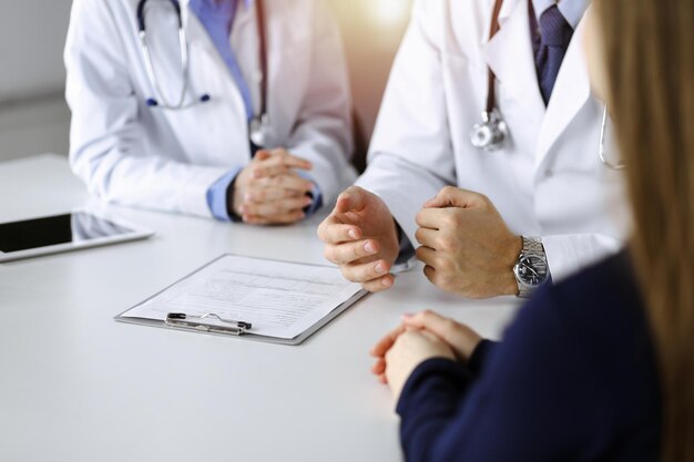 Médico desconhecido ouvindo sua mulher paciente enquanto está sentado na clínica ensolarada. Conceito de medicina durante a pandemia de Coronavirus. Covid 2019.