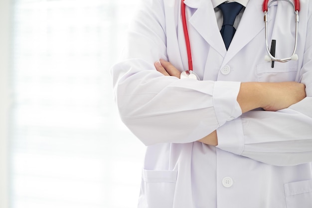 Médico desconhecido posando com os braços cruzados no escritório, ele está usando um estetoscópio