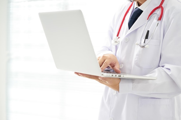 Médico desconhecido posando usando laptop com fundo brilhante, ele está usando um estetoscópio