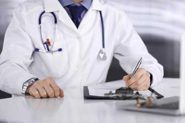 Médico desconhecido sentado e trabalhando com prancheta de registro de histórico de medicação na clínica em seu local de trabalho, close-up. Jovem médico no trabalho. Serviço médico perfeito, conceito de medicina.