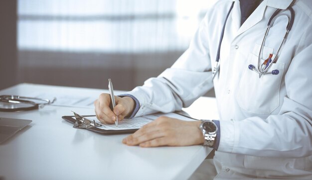 Médico desconhecido sentado e trabalhando com prancheta de registro de histórico de medicação na clínica em seu local de trabalho, close-up. Jovem médico no trabalho. Serviço médico perfeito, conceito de medicina.