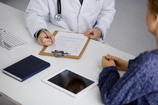 Foto médico desconocido de barba roja y mujer paciente discutiendo el examen de salud actual mientras está sentado en una clínica soleada, de cerca. concepto de medicina.