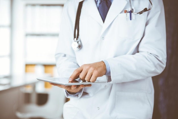 Médico desconocido de barba roja y mujer paciente discutiendo el examen de salud actual mientras se sienta y usa una tableta en la clínica, de cerca. concepto de medicina.