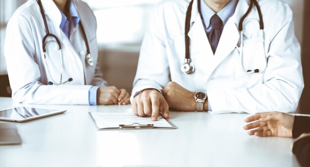 Un médico desconocido escucha a su paciente mientras se sienta en una clínica moderna. Servicio médico perfecto, concepto de medicina durante la pandemia del Coronavirus. covid 2019.