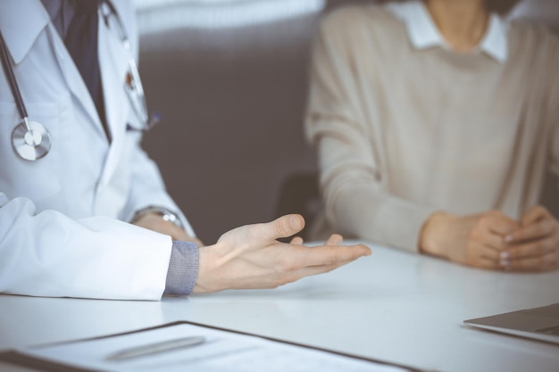 Un médico desconocido y una mujer paciente discutiendo algo mientras estaban sentados en la clínica. Mejor servicio médico en hospital, medicina, parada pandémica