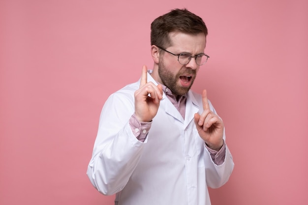 Un médico descontento con una bata blanca regaña a alguien que señala estrictamente con los dedos Fondo rosa