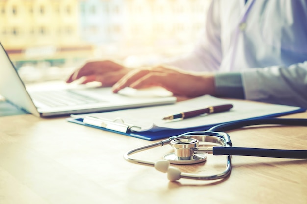 Médico digitando informações no laptop no escritório do hospital foco em estetoscópio