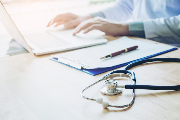 Médico digitando informações no laptop no escritório do hospital foco em estetoscópio