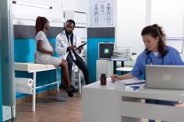 Médico discutiendo con la paciente embarazada sobre la atención médica y el embarazo para dar tratamiento y medicamentos recetados. Mujer esperando un niño en la cita, hablando con un especialista.