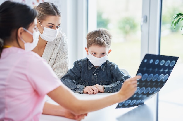 Médico discutindo resultados de raios-x com a mãe e seu filho, todos usando máscaras devido ao covid-19