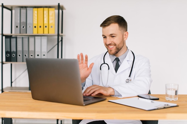 Médico do sexo masculino feliz assistindo a um webinar médico online ou seminário de treinamento enquanto está sentado com um laptop no local de trabalho