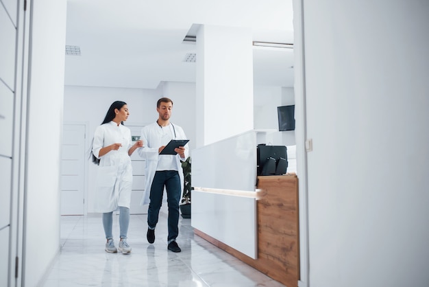 Médico e enfermeira morena caminham no hospital e conversam no trabalho.